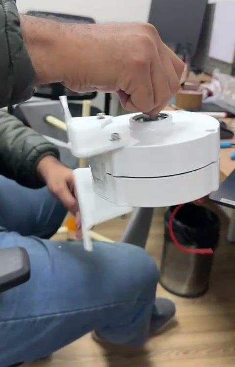 Hands holding the small imported generator at a desk: a white housing on a stub of shaft.