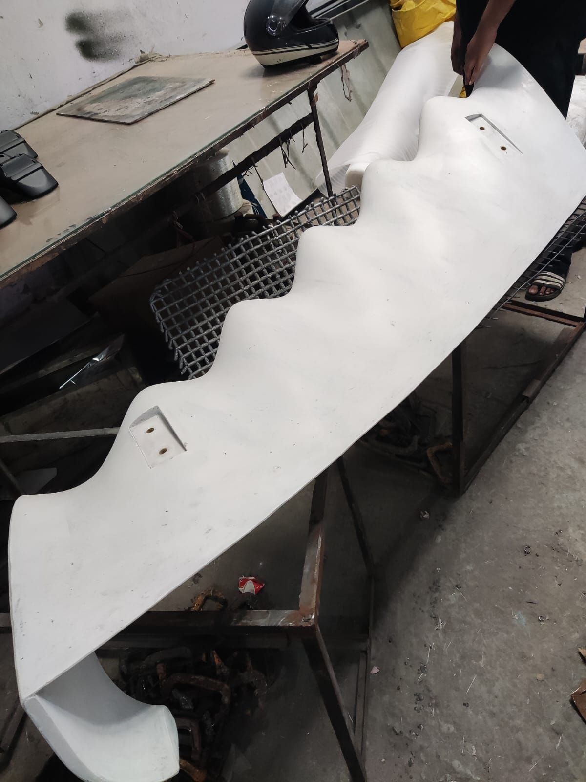 The first white composite blade lying on a workshop bench, its wavy edge catching the light.
