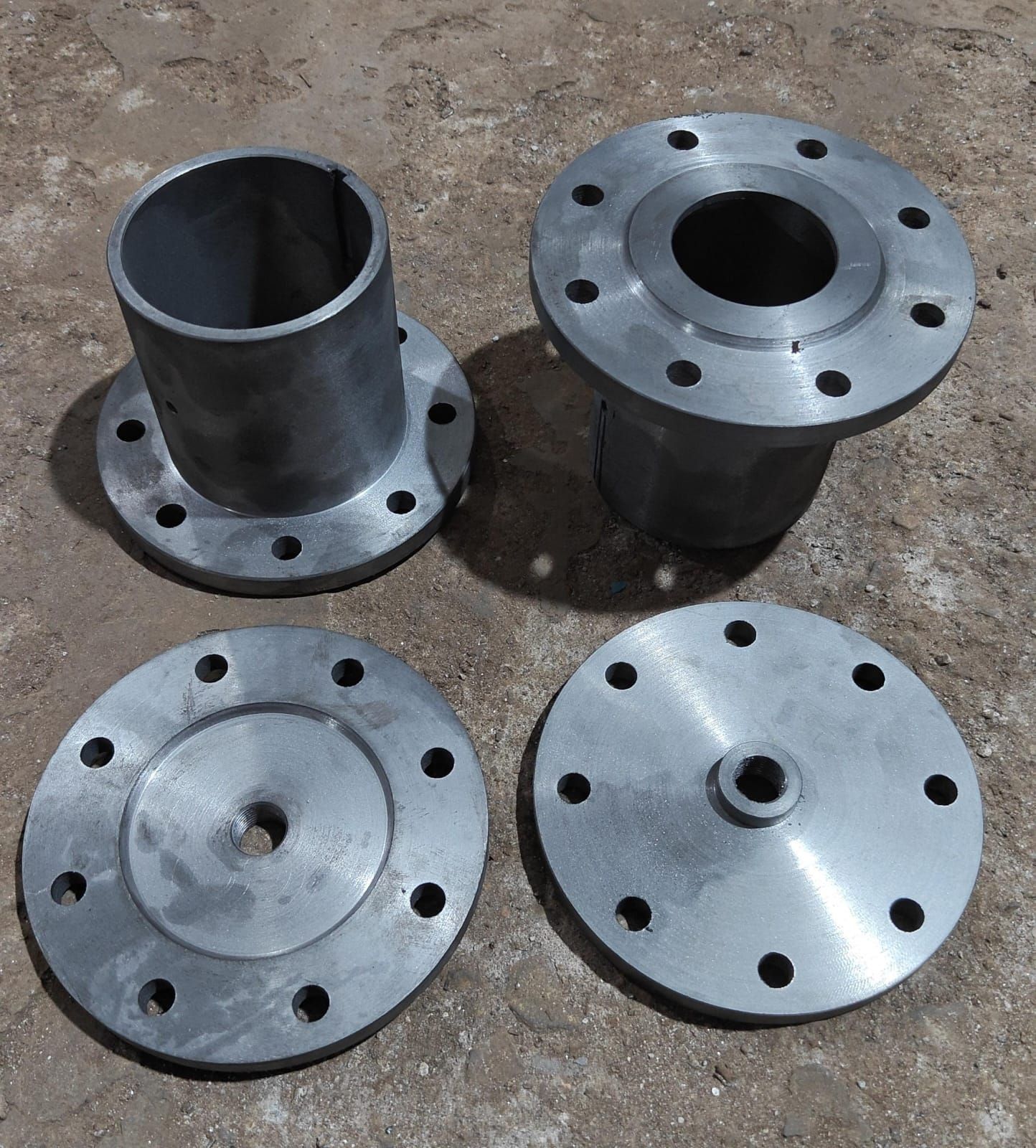 Four machined hub and flange parts laid out on the ground.