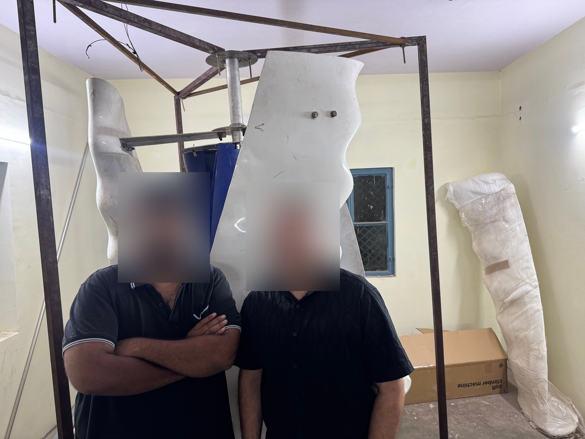 Two of the team standing in front of the first full assembly inside its steel rig, faces blurred.