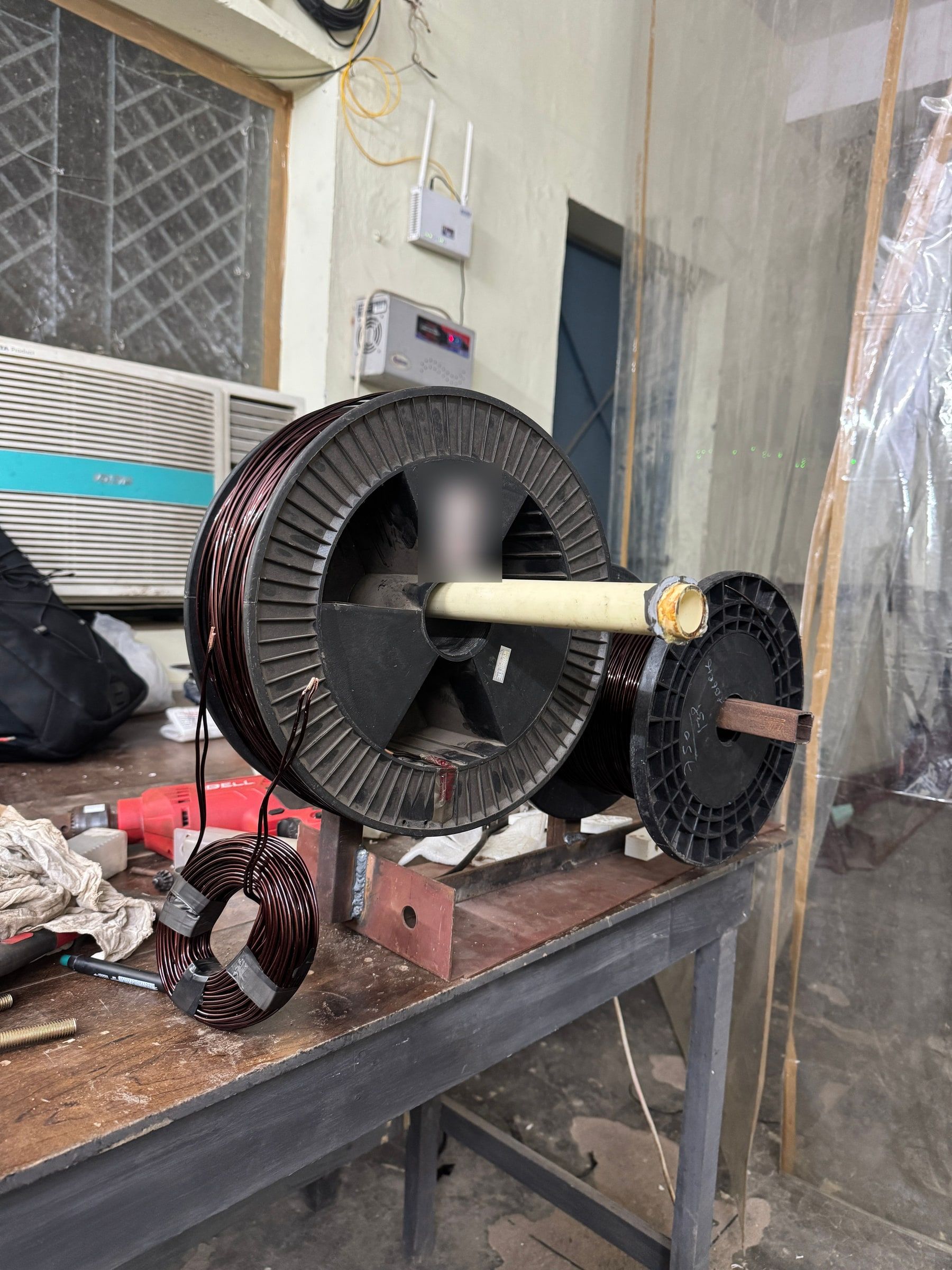 A spool of enamelled copper magnet wire on the workbench beside a finished coil.