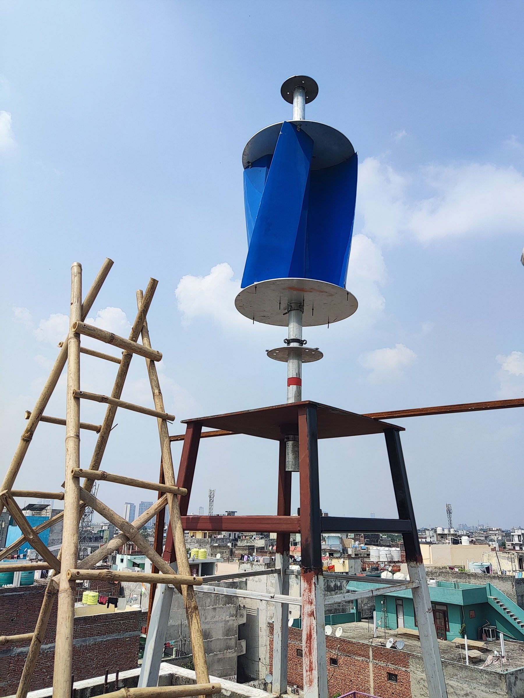 The rotor mounted at the top of the stand against the sky, seen from below, above the rooftop line.