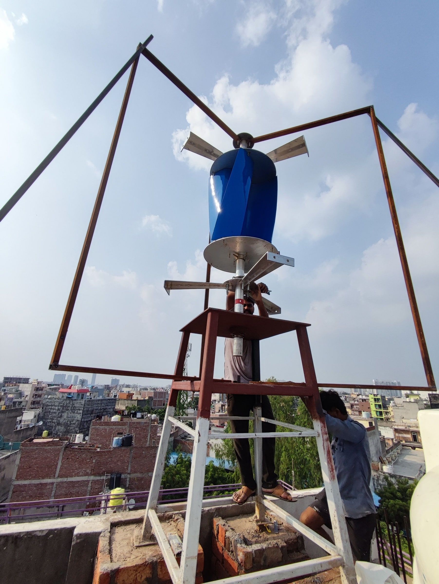 The tall steel stand raised on the rooftop, rotor mounted at the top, two people fitting it.
