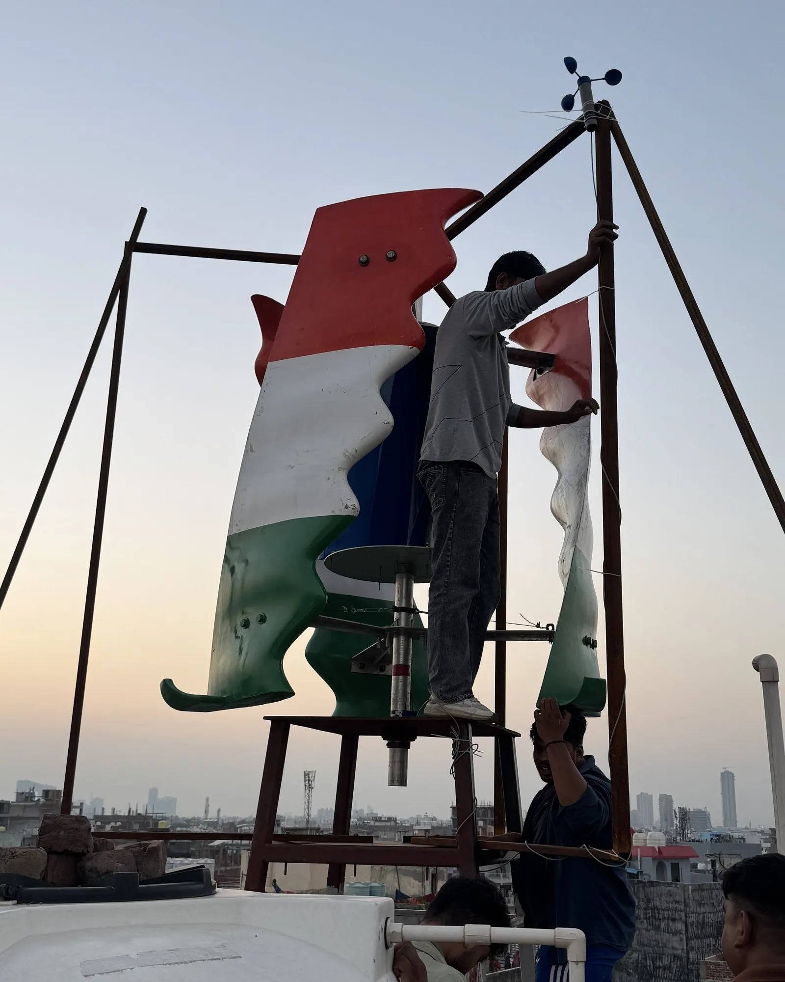 GIVARA ONE in tricolour at golden hour on its first rooftop, a crew member fitting the anemometer mast, September 2026.